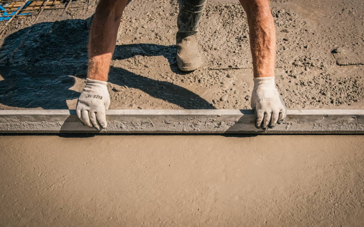 Mains d'un homme en train de lisser le béton sur un chantier d'Enrico Baiutti SA.